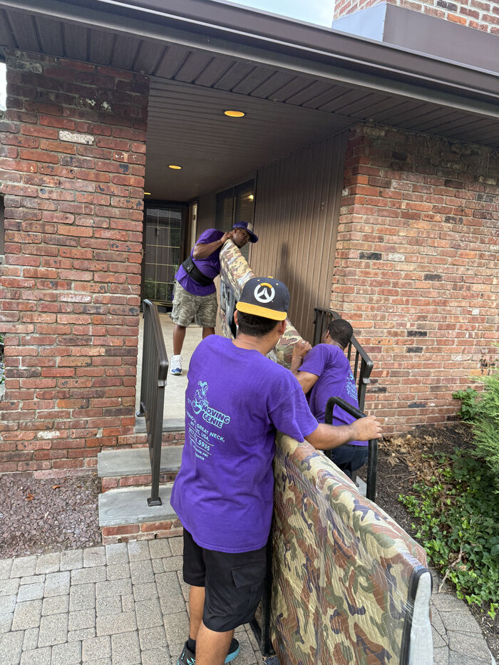 Movers carrying a couch up brick steps outside a Long Island City building