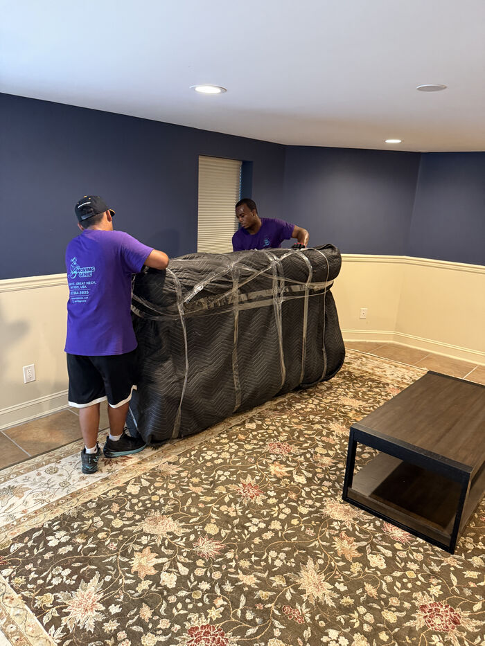 The Moving Genie crew wrapping and padding furniture in a room before loading it onto the truck