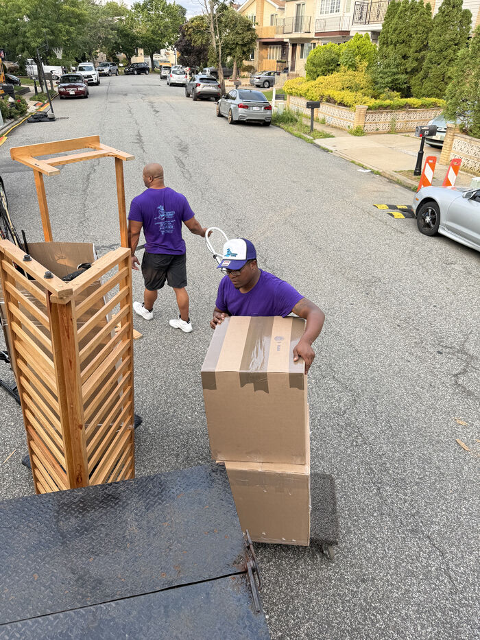 A hand truck stacked with labeled moving boxes on a New York City sidewalk outside an apartment building