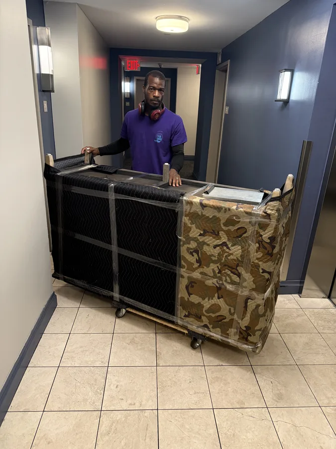 Mover guiding padded furniture on dollies through a building hallway