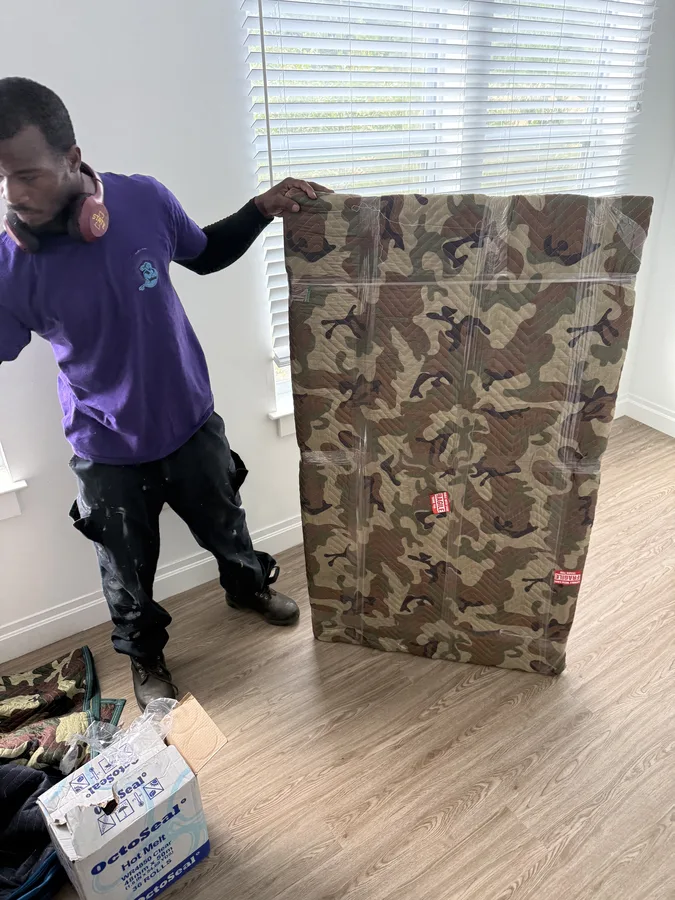 Mover beside a furniture panel protected with a moving blanket and straps