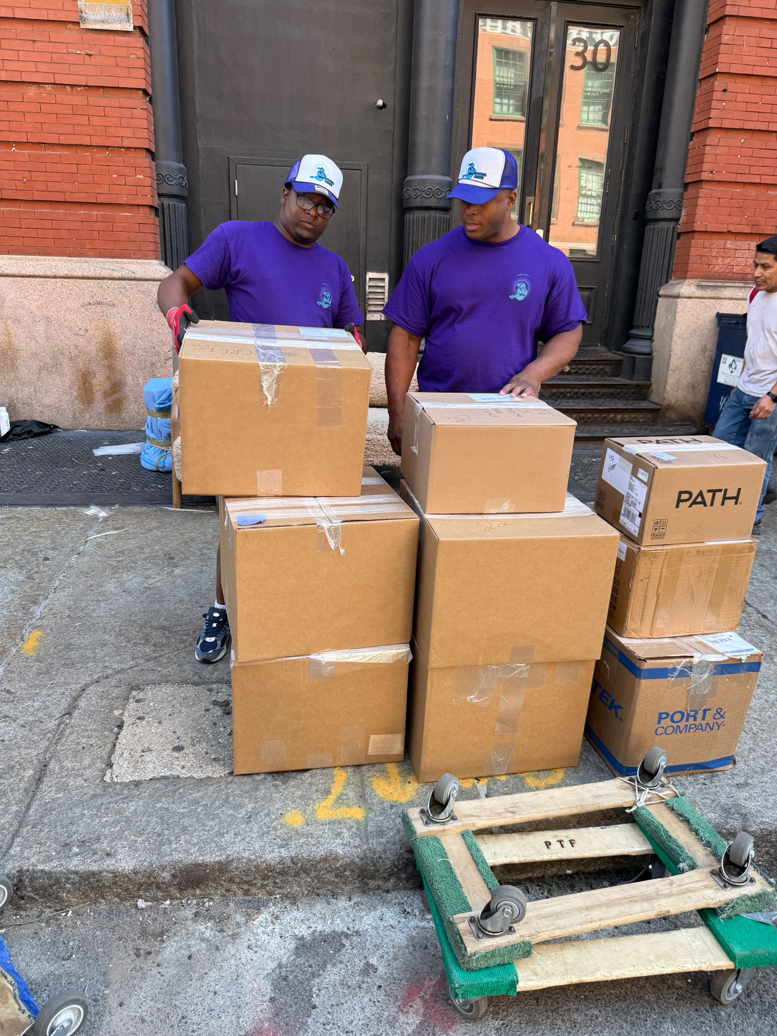 The Moving Genie crew in branded purple shirts loading boxes onto a dolly on a New York City street